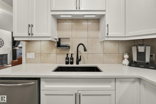 White shaker-style cabinetry, light-toned countertop, square tiled backsplash, black basin sink, and matte black gooseneck faucet - #9 175 Mcconachie Dr Nw, Edmonton, AB 