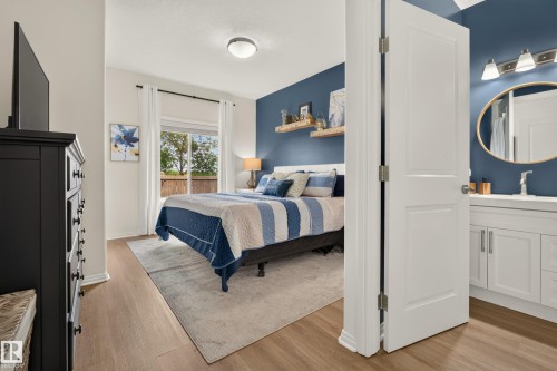 Wood-finish flooring throughout, a sliding glass door, a bathroom vanity with integrated sink, and an oval wall mirror - #9 175 Mcconachie Dr Nw, Edmonton, AB 