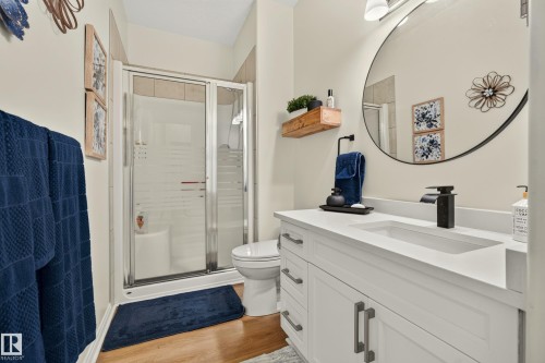 Bathroom featuring wood-finish flooring, a white vanity with an integrated sink, a dark-toned faucet, and a glass-enclosed shower - #9 175 Mcconachie Dr Nw, Edmonton, AB 