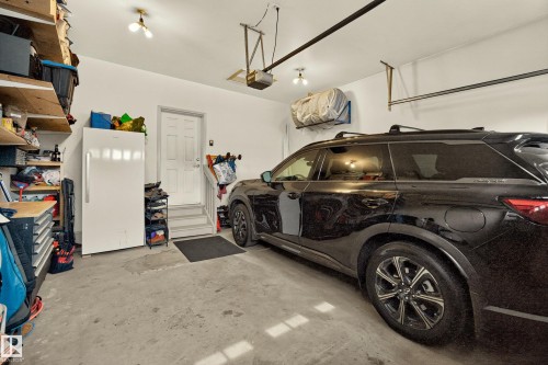 Concrete flooring garage with an overhead door opener, interior access door, and integrated shelving - #9 175 Mcconachie Dr Nw, Edmonton, AB 
