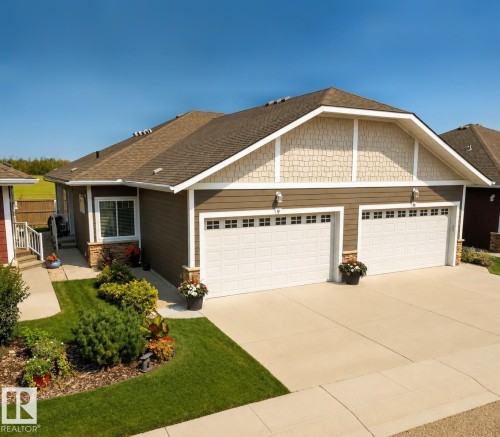 Two-car garage with white panel doors, accented by stone veneer and decorative shaker siding - #9 175 Mcconachie Dr Nw, Edmonton, AB 