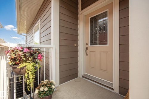 Siding exterior with white trim, leading to a front entry door with decorative glass paneling - #9 175 Mcconachie Dr Nw, Edmonton, AB 