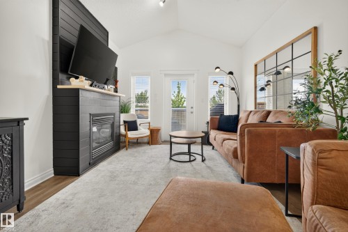 Vaulted ceiling, gas fireplace with wood mantel, wood-finish flooring, white walls, and glass-paned door - #9 175 Mcconachie Dr Nw, Edmonton, AB 
