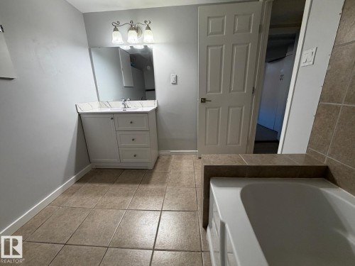 White vanity with a single sink, three-bulb vanity light, and a large wall mirror - 4708 117A Street Northwest, Edmonton, AB 