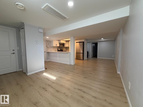 Open concept living area featuring wood-finish flooring, recessed lighting, and a kitchen with white cabinetry and stainless steel appliances - 4708 117A Street Northwest, Edmonton, AB 