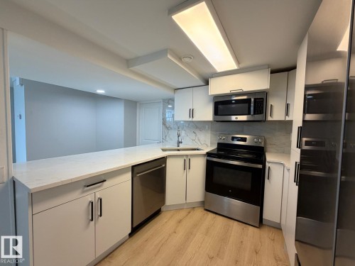 Kitchen featuring white cabinetry, stainless steel appliances, a white countertop, and a tiled backsplash - 4708 117A Street Northwest, Edmonton, AB 