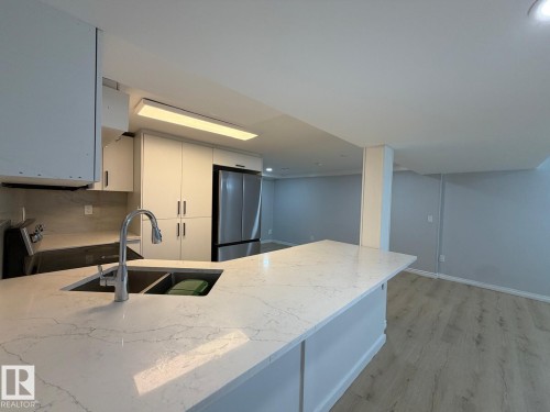Kitchen featuring a dual basin sink, pull-down faucet, white cabinetry, integrated stainless steel refrigerator, and light-toned wood-finish flooring - 4708 117A Street Northwest, Edmonton, AB 