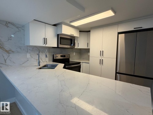 White flat-panel cabinetry, stainless steel appliances, stainless steel sink with gooseneck faucet, light-toned countertop, and patterned backsplash - 4708 117A Street Northwest, Edmonton, AB 
