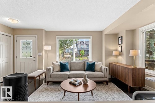 Living area with dark wood-finish flooring, light neutral wall paint, and multiple windows - 5319 3 Avenue Sw, Edmonton, AB 