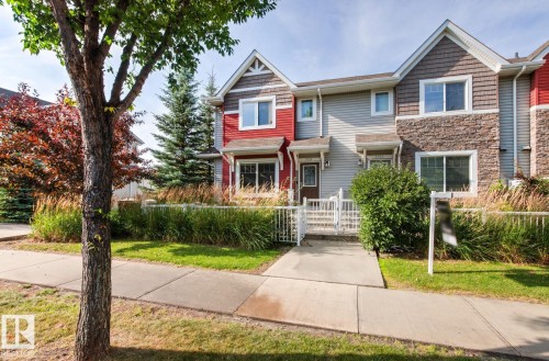 Townhome exterior featuring horizontal siding, decorative stone cladding, and a white picket fence - 5319 3 Avenue Sw, Edmonton, AB 
