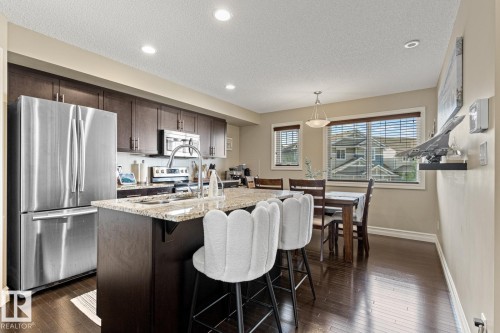 Kitchen featuring dark wood-finish flooring, dark cabinetry, stainless steel appliances, a kitchen island with a built-in sink, and recessed lighting - 5319 3 Avenue Sw, Edmonton, AB 