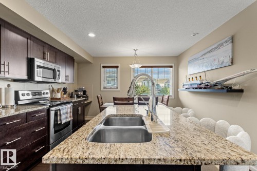 Kitchen featuring granite countertops, dark wood-finish cabinetry, stainless steel appliances, and a double basin sink with a high-arc faucet - 5319 3 Avenue Sw, Edmonton, AB 