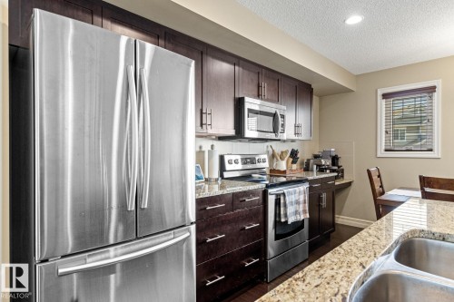 Kitchen featuring stainless steel appliances, dark wood cabinetry, and granite-style countertops - 5319 3 Avenue Sw, Edmonton, AB 