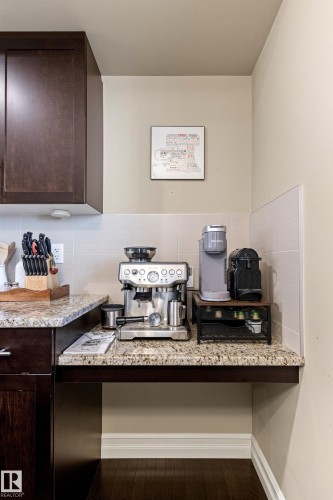 Granite-finish countertop, dark wood-finish cabinetry, tile backsplash, built-in desk or workstation, and wood-finish flooring - 5319 3 Avenue Sw, Edmonton, AB 