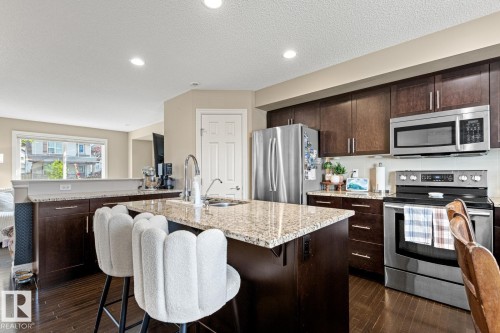 Kitchen featuring dark wood-finish cabinetry, light speckled countertops, stainless steel appliances, and a central island with an undermount sink - 5319 3 Avenue Sw, Edmonton, AB 