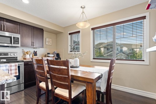 Kitchen and dining area featuring stainless steel appliances, dark wood-finish cabinetry, a large window, and dark wood-finish flooring - 5319 3 Avenue Sw, Edmonton, AB 