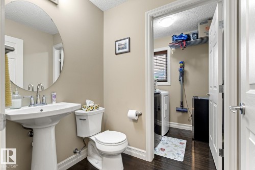 Pedestal sink with chrome faucet, oval mirror, and a toilet with a dual-flush mechanism - 5319 3 Avenue Sw, Edmonton, AB 