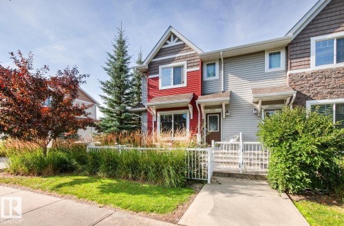 Townhome exterior featuring red and grey siding, stone accents, multiple windows, a concrete walkway, and a white fence - 5319 3 Avenue Sw, Edmonton, AB 