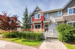 Townhome exterior featuring red and grey siding, stone accents, multiple windows, a concrete walkway, and a white fence - 