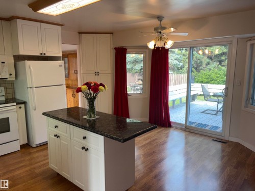 Kitchen featuring wood-finish flooring, white cabinetry, a kitchen island with a dark countertop, a ceiling fan, and sliding glass doors opening to an exterior deck - 4027 74 Street Nw, Edmonton, AB 