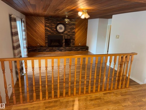 Wood-finish flooring throughout, wood-paneled ceiling, brick fireplace with mantel, wood-paneled accent wall, and decorative wood railing - 4027 74 Street Nw, Edmonton, AB 