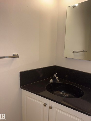 White vanity cabinetry with polished chrome hardware, dark stone countertop, integrated black oval sink, and wall-mounted mirror - 4027 74 Street Nw, Edmonton, AB 