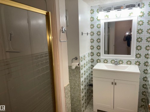 Vanity with white cabinetry and integrated sink, chrome faucet, wall-mounted mirror, and decorative tiled walls - 4027 74 Street Nw, Edmonton, AB 