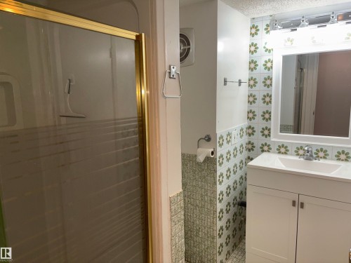 White vanity with an integrated sink and chrome faucet, framed mirror with overhead lighting, and patterned wall tiling - 4027 74 Street Nw, Edmonton, AB 