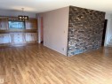 Wood-finish flooring throughout, featuring built-in cabinetry with a window, a contemporary chandelier, and a brick accent wall - 4027 74 Street Nw, Edmonton, AB 