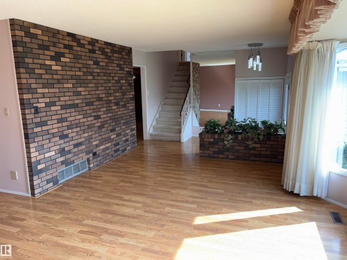Wood-finish flooring, accent brick wall, staircase with metal railing, bay window, and a built-in brick planter - 4027 74 Street Nw, Edmonton, AB 