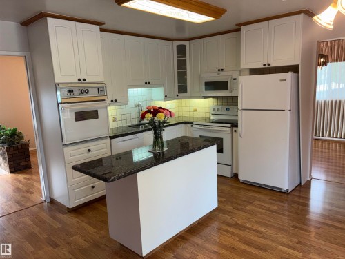 White cabinetry with wood-finish trim, built-in oven, granite-finish countertops, wood-finish flooring, and a central island - 4027 74 Street Nw, Edmonton, AB 