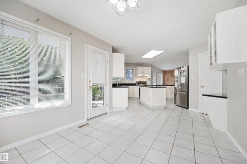 Kitchen with white tiled flooring, white cabinetry, dark countertops, and stainless steel refrigerator - 5107 17 Avenue Nw, Edmonton, AB 