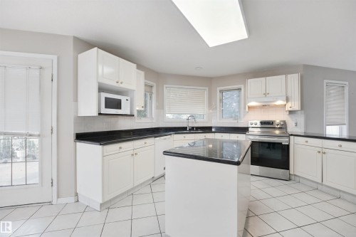White cabinetry with dark countertops, a kitchen island, tile flooring, and a stainless steel oven - 5107 17 Avenue Nw, Edmonton, AB 