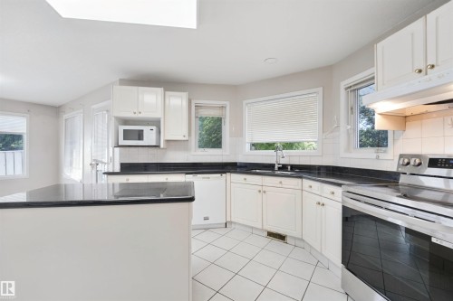 White cabinetry, dark countertops, tile flooring, built-in microwave, and stainless steel range - 5107 17 Avenue Nw, Edmonton, AB 