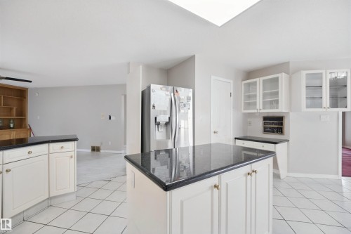 Kitchen featuring a central island, white cabinetry, dark countertops, a skylight, and tiled flooring - 5107 17 Avenue Nw, Edmonton, AB 