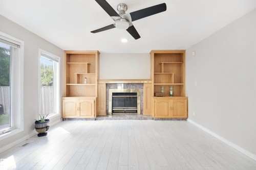 Light wood-finish flooring, built-in shelving, stone fireplace surround, and a ceiling fan with integrated lighting - 5107 17 Avenue Nw, Edmonton, AB 