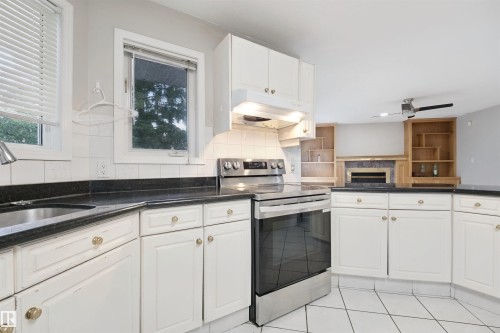 Kitchen featuring white cabinetry, dark countertops, white tile flooring, stainless steel range, and an integrated sink - 5107 17 Avenue Nw, Edmonton, AB 