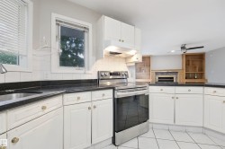 Kitchen featuring white cabinetry, dark countertops, white tile flooring, stainless steel range, and an integrated sink - 