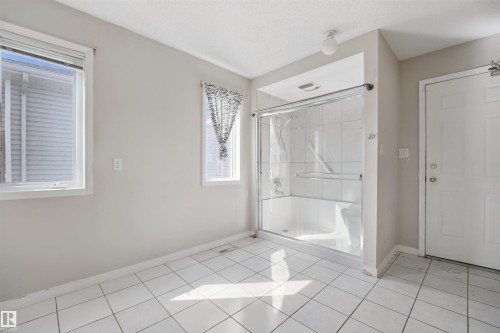 Tub/shower combination with sliding glass enclosure, white tile flooring, and multiple windows - 5107 17 Avenue Nw, Edmonton, AB 