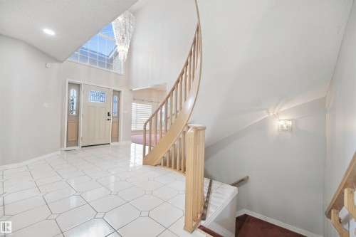 Two-story entryway with white tile flooring, curved wooden staircase, and transom windows - 5107 17 Avenue Nw, Edmonton, AB 
