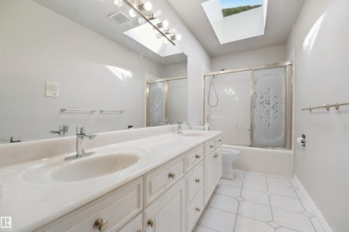 Dual vanity with integrated sinks, full-width mirror, overhead lighting fixture, and a skylight - 5107 17 Avenue Nw, Edmonton, AB 