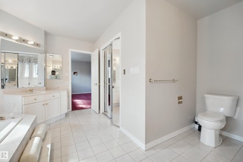 White tiled flooring, dual vanities with integrated sinks, mirrored sliding closet doors, and a built-in bathtub - 5107 17 Avenue Nw, Edmonton, AB 