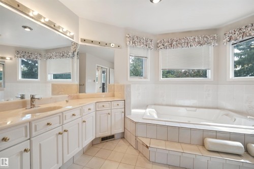 Dual vanity with integrated sinks, expansive mirror, tiled flooring, built-in soaking tub, and multiple windows - 5107 17 Avenue Nw, Edmonton, AB 