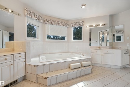 Built-in soaking tub with tiled surround, dual vanity with undermount sinks, tiled flooring, and multiple windows - 5107 17 Avenue Nw, Edmonton, AB 