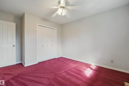 Room featuring a ceiling fan, white paneled doors, and red patterned carpeting - 5107 17 Avenue Nw, Edmonton, AB 