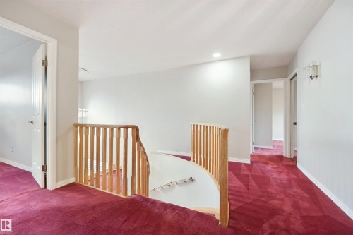 Hardwood railing with spindle design, recessed lighting, wall-mounted sconce, light gray wall finishes, and red pattern carpeting - 5107 17 Avenue Nw, Edmonton, AB 