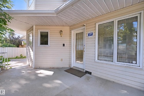 Covered concrete patio with white vinyl siding, multiple windows, and exterior lighting fixture - 5107 17 Avenue Nw, Edmonton, AB 
