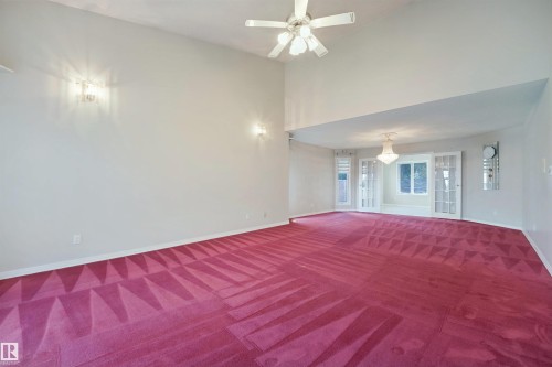 Vaulted ceiling with ceiling fan, recessed area with chandelier, dual French doors, and patterned carpet - 5107 17 Avenue Nw, Edmonton, AB 