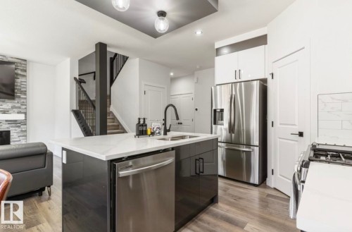 Open-concept kitchen featuring an island with integrated sink, stainless steel appliances, and wood-finish flooring - 19703 29 Avenue Nw, Edmonton, AB 