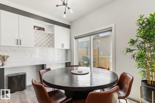Contemporary lighting fixture, white upper cabinetry with black hardware, integrated wine rack, white subway tile backsplash, and sliding glass door - 19703 29 Avenue Nw, Edmonton, AB 